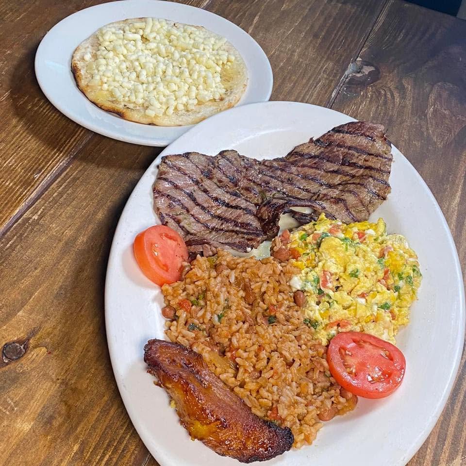 Grilled steak with scrambled eggs and hogao, rice, a corn arepa and a sweet plantain on a white platter