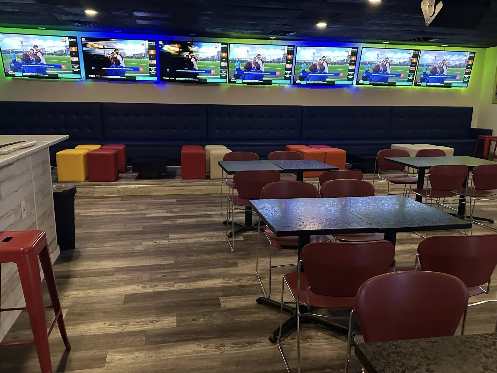 Lounge seating with red stools and a wall of screens