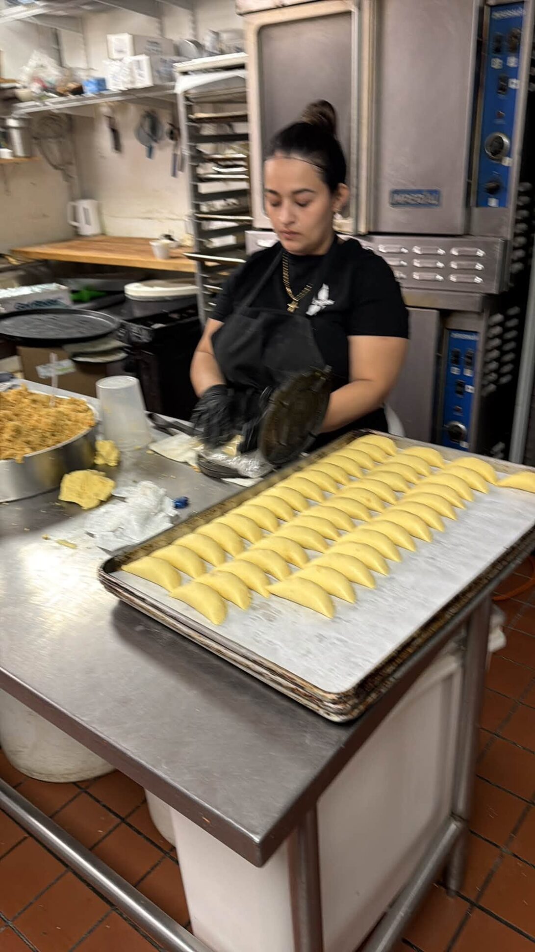 A baker laying out a sheet pan of raw empanadas in the kitchen