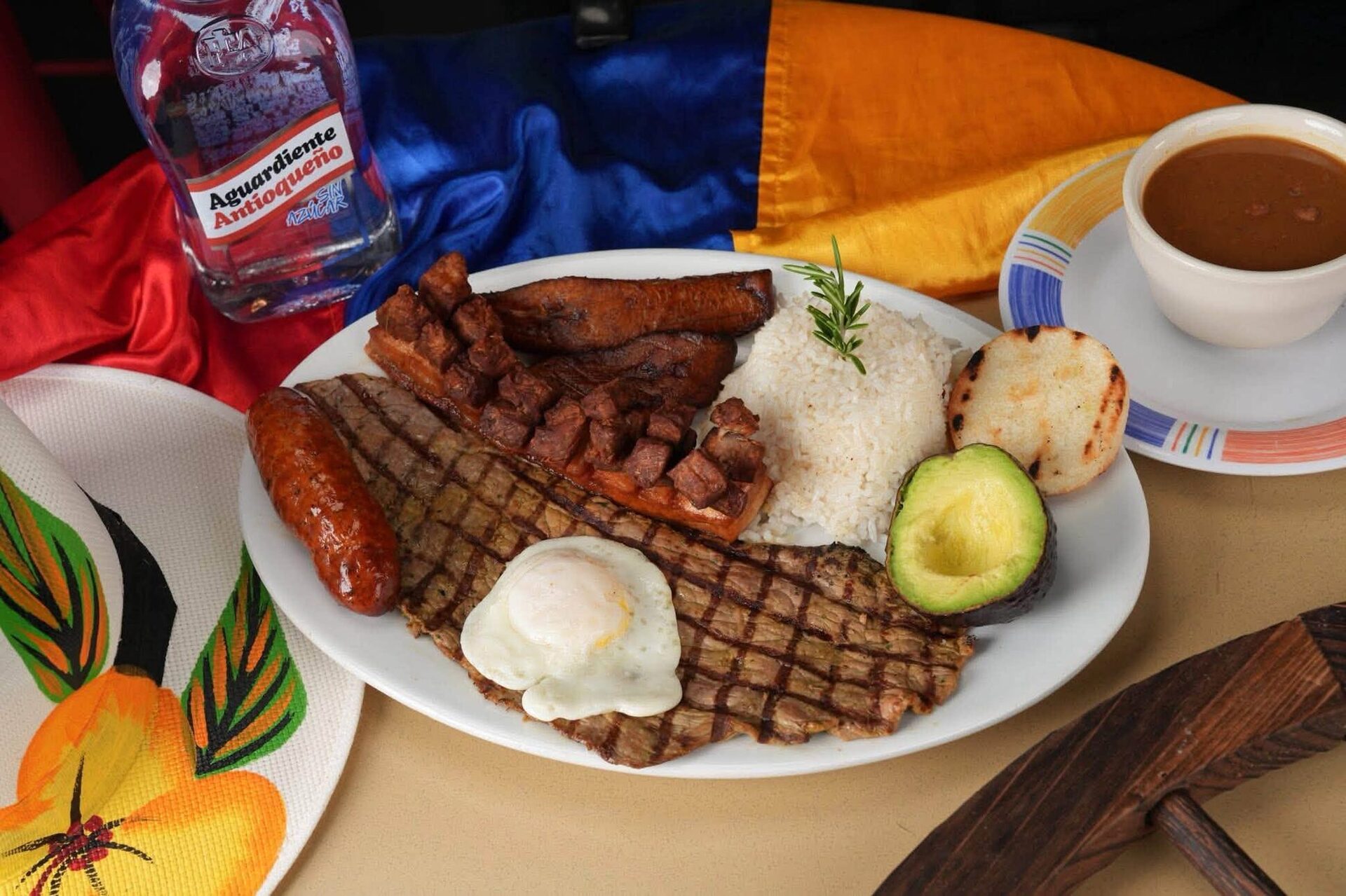 A grilled-steak bandeja with chorizo, egg and avocado on a table draped with the Colombian flag