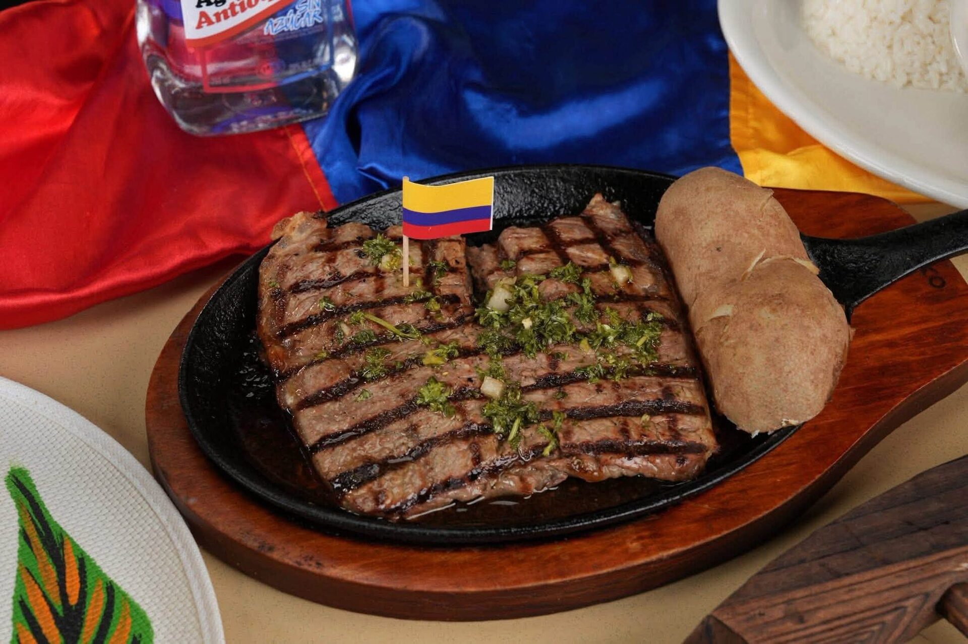 Grilled churrasco on a sizzling skillet with a small Colombian flag pick and a baked potato