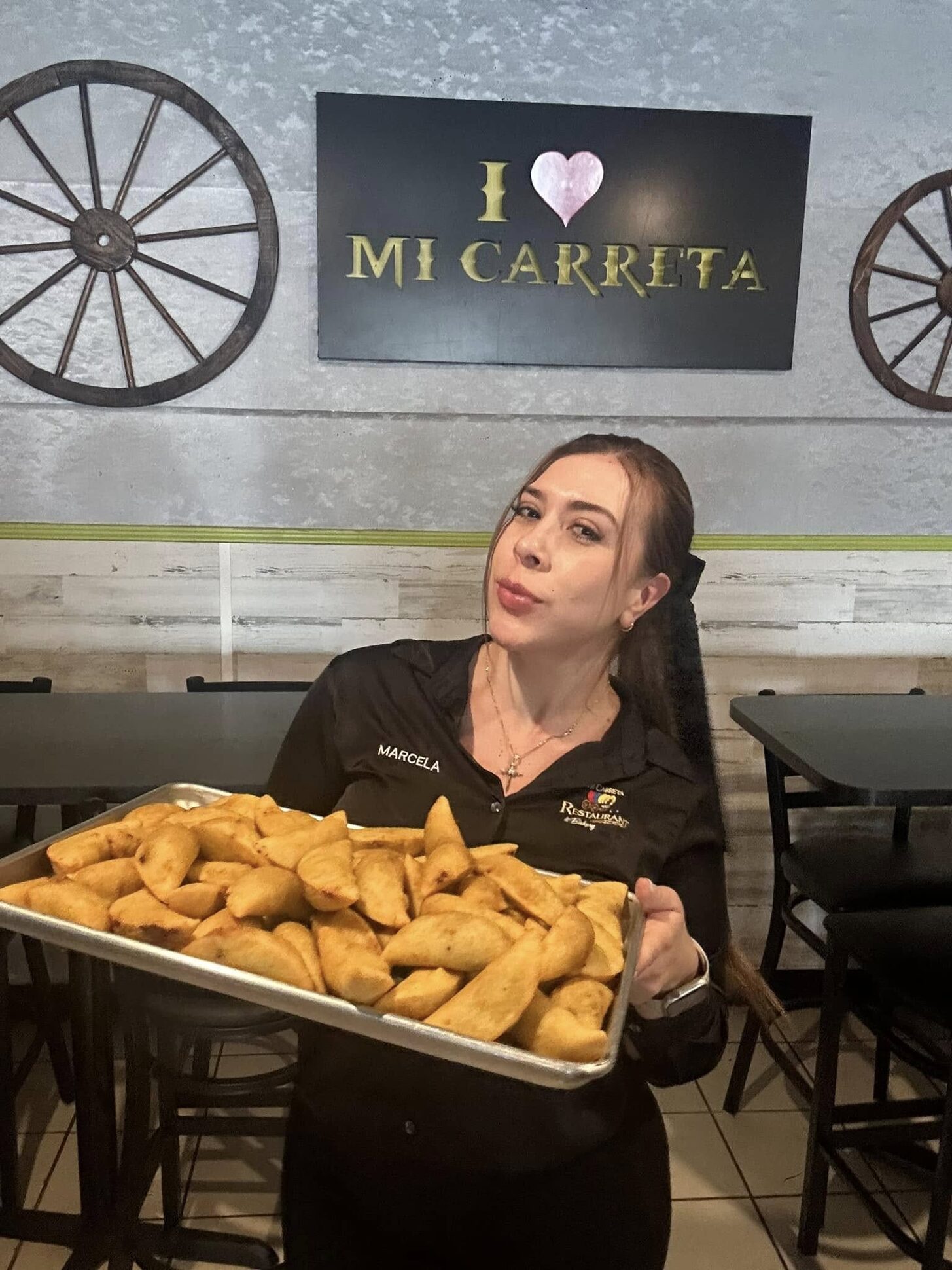 A Mi Carreta team member holding a tray of empanadas under the I love Mi Carreta sign
