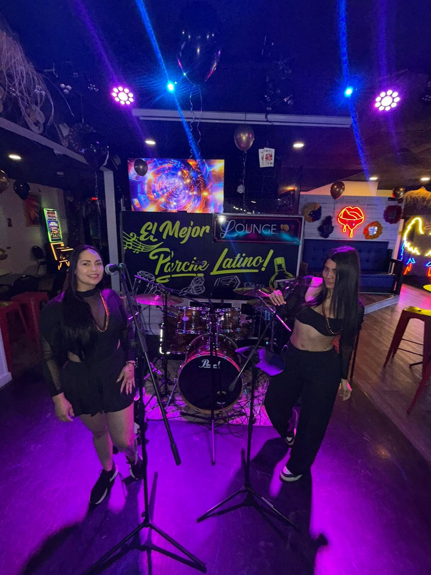 Two singers on the Lounge stage in violet light under the El Mejor Parche Latino sign