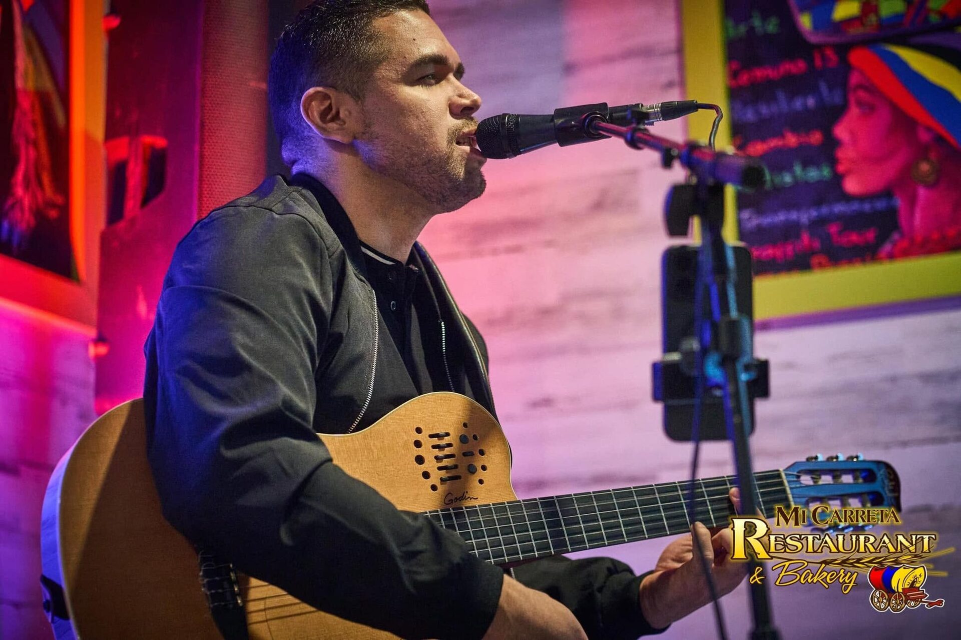 A singer with an acoustic guitar under pink and violet stage light