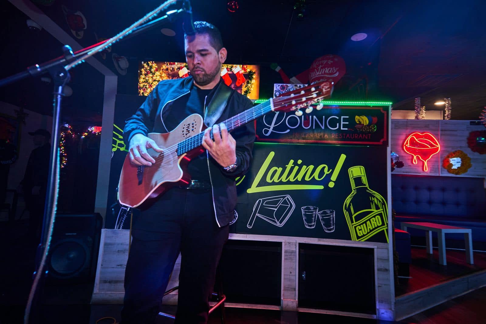 A guitarist performing in front of the neon Lounge sign