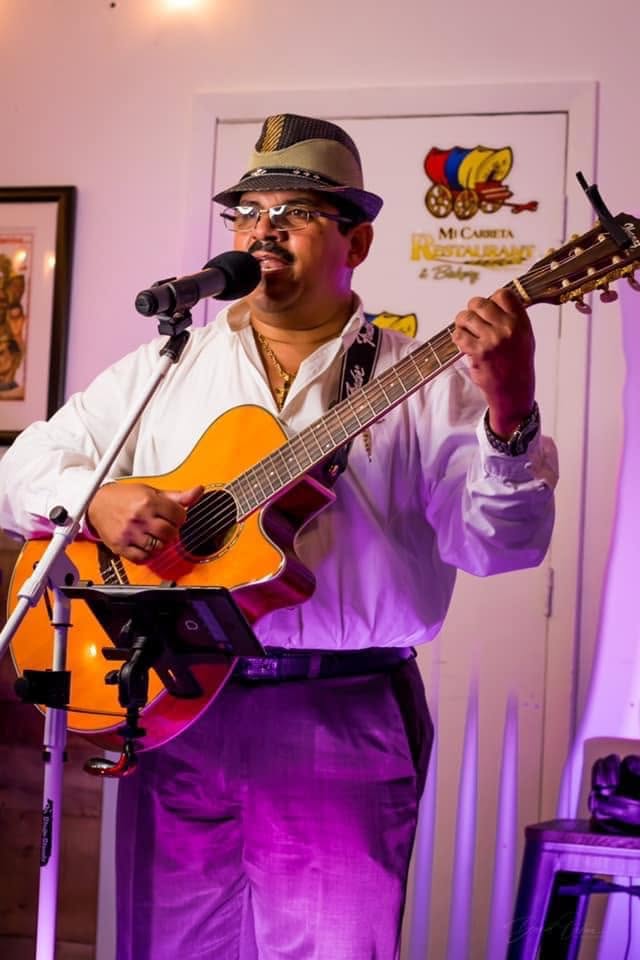 A singer in a sombrero vueltiao playing guitar under violet light