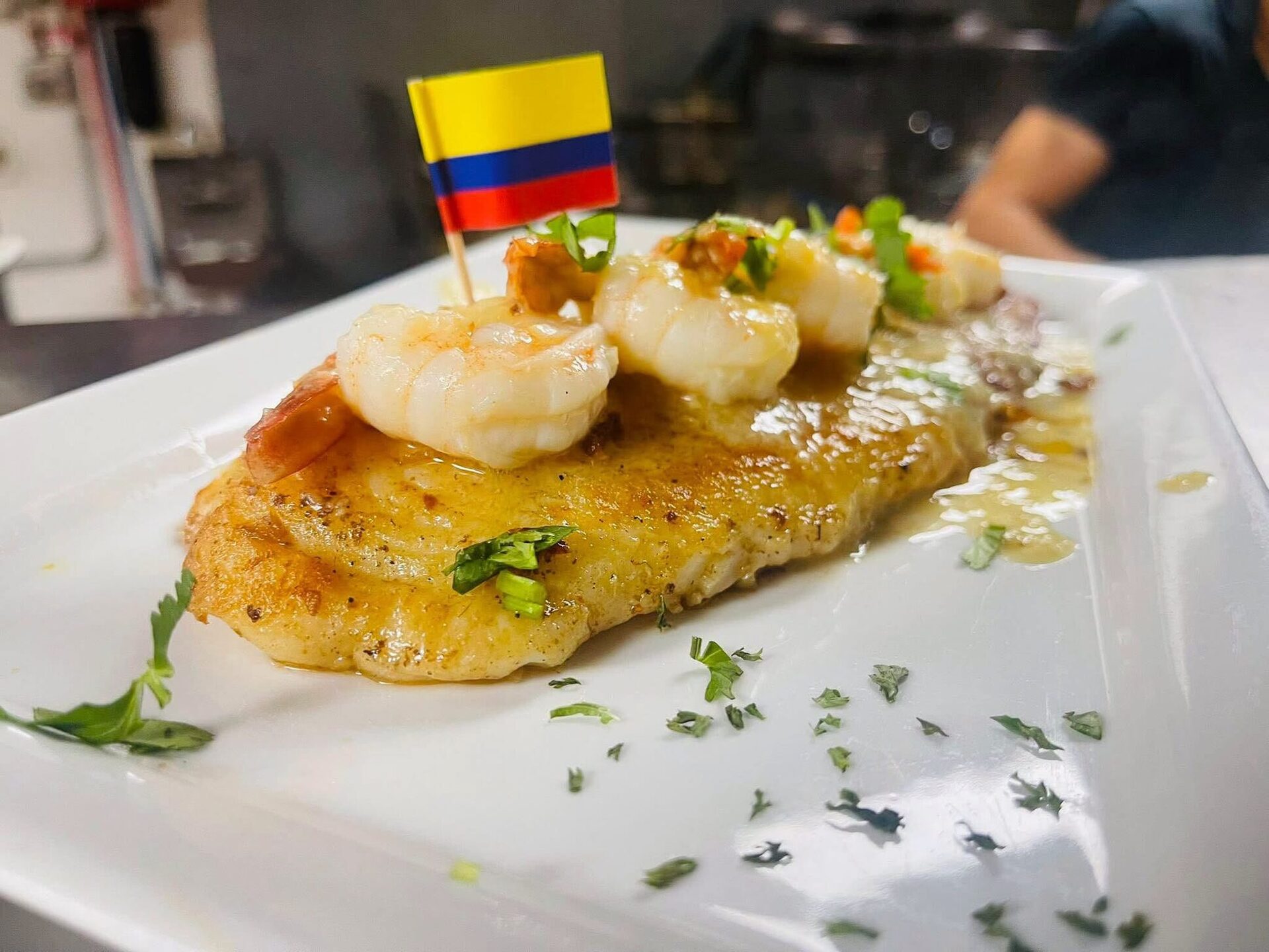 A fish fillet topped with shrimp and a Colombian flag pick