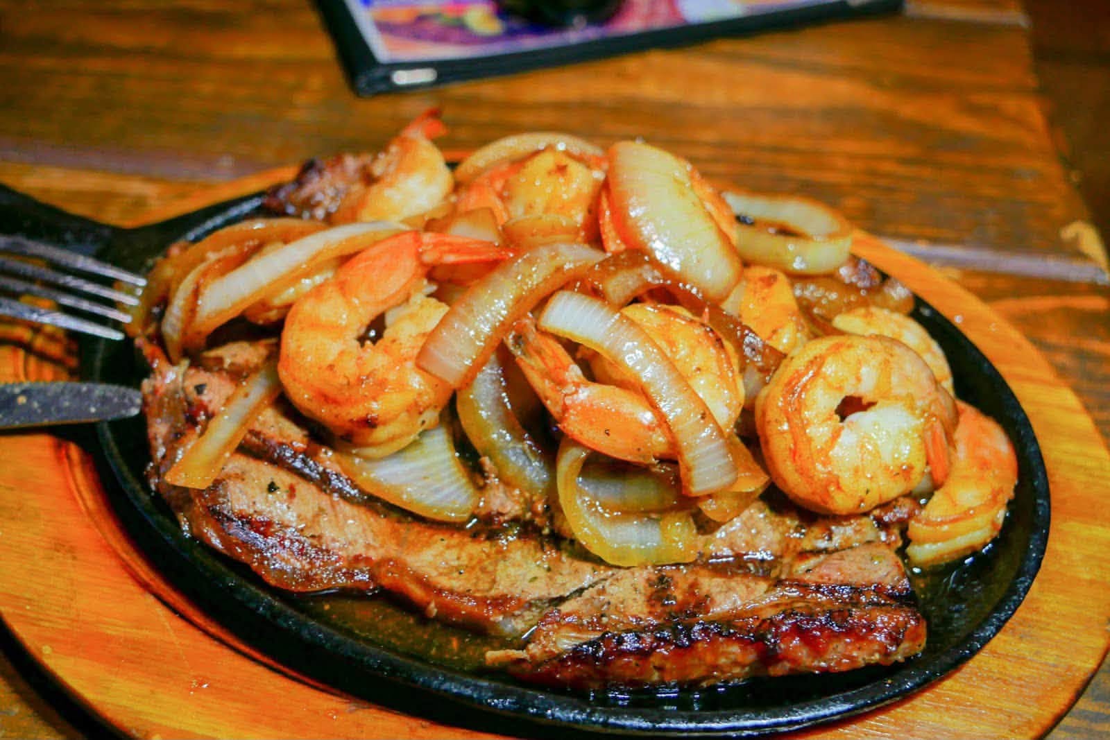 Shrimp and steak sizzling with onions on a cast-iron platter