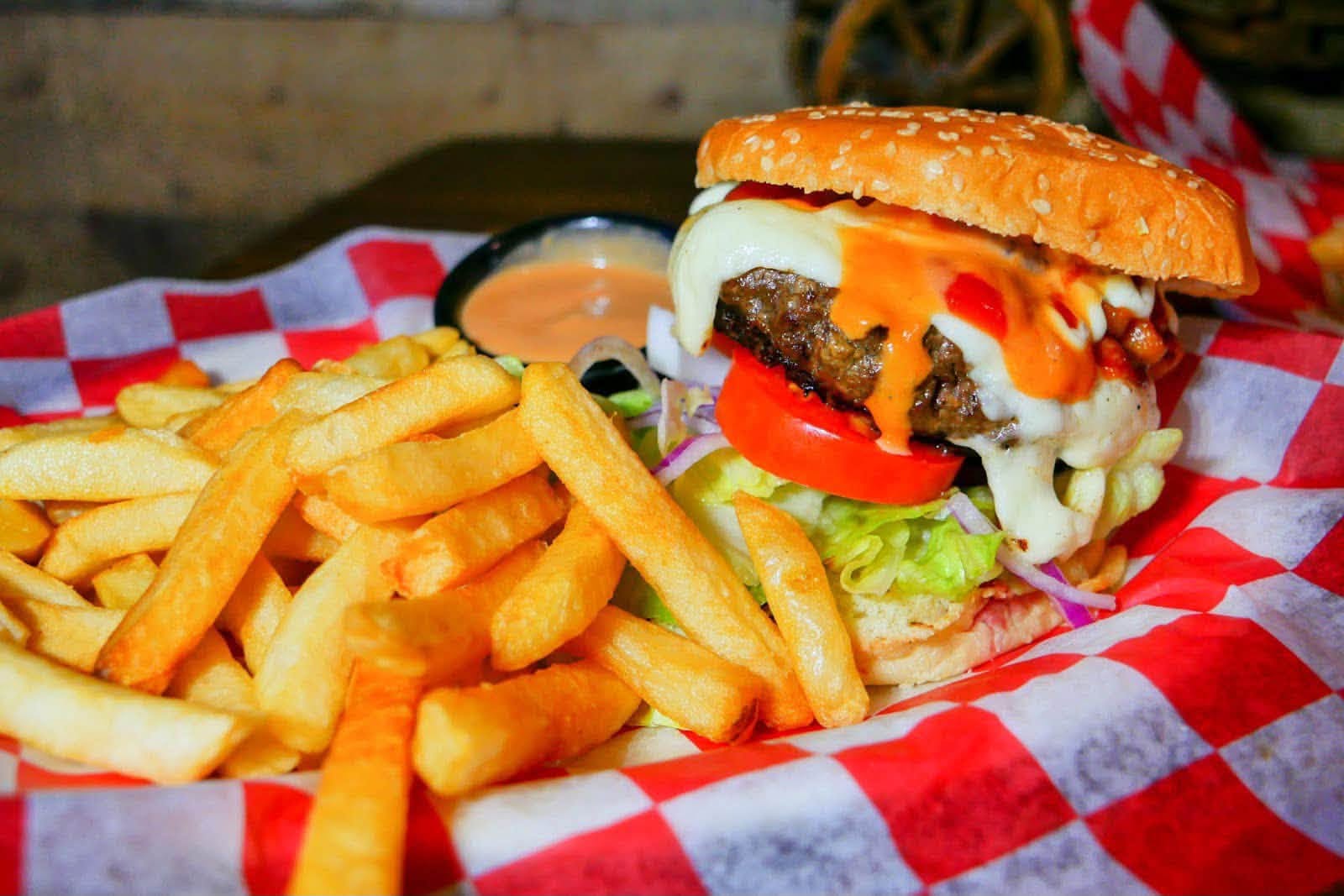A bacon cheeseburger and fries in a red-checked basket