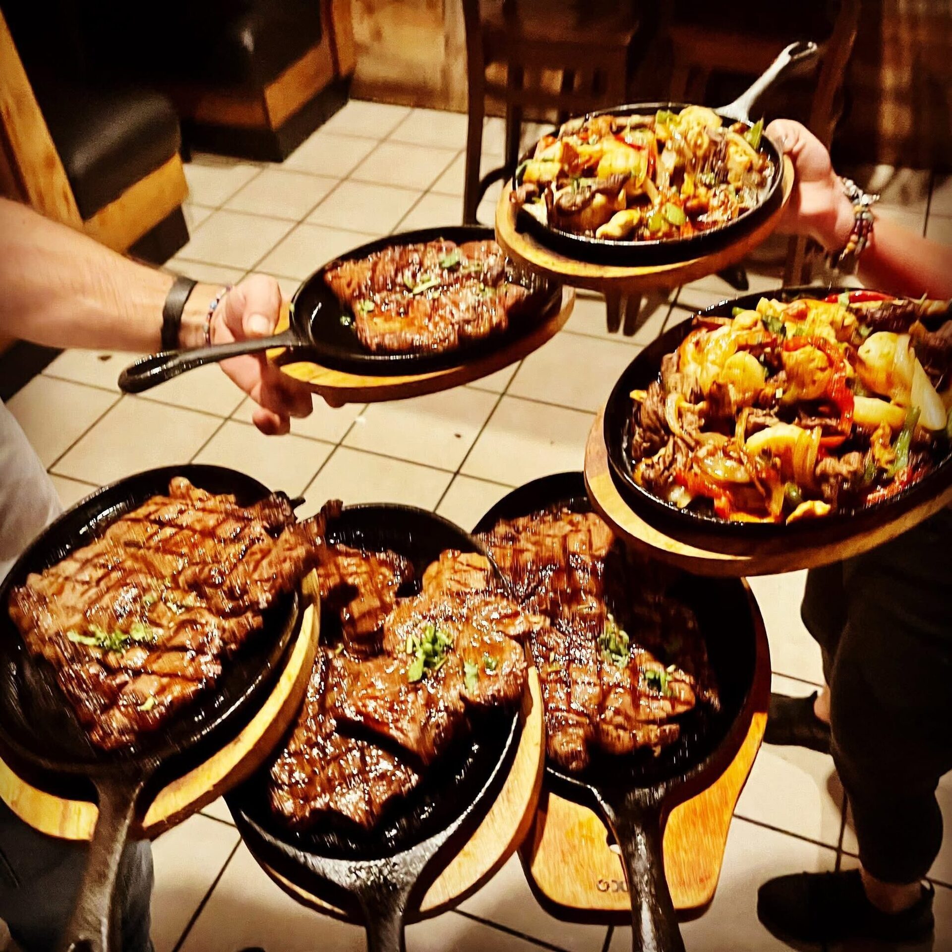 Servers carrying five sizzling cast-iron platters of steak and fajitas across the tile floor