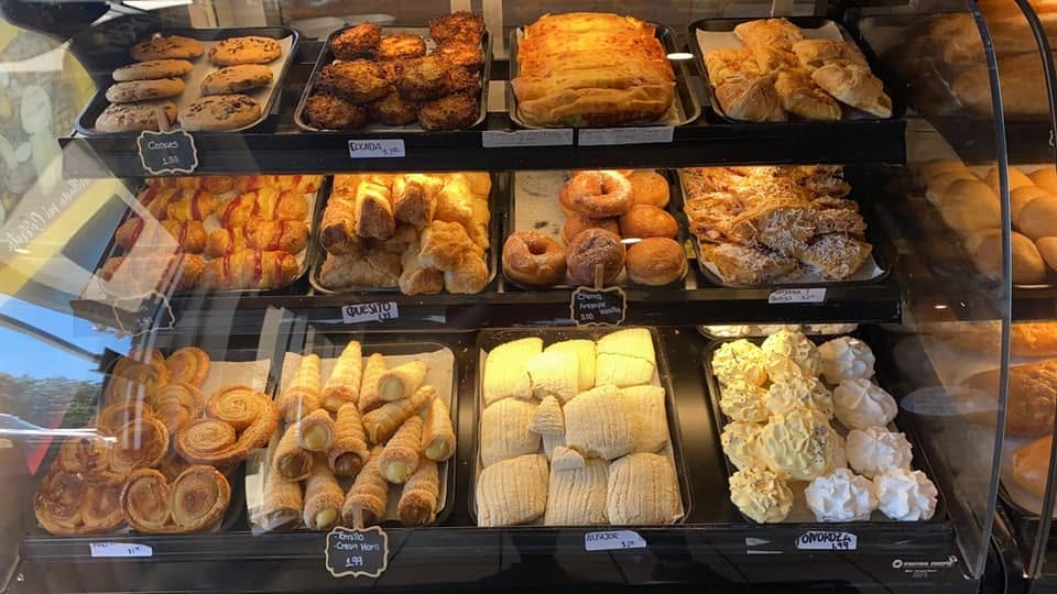 Three shelves of the bakery case: cream cones, puff pastries, almojábanas and meringues