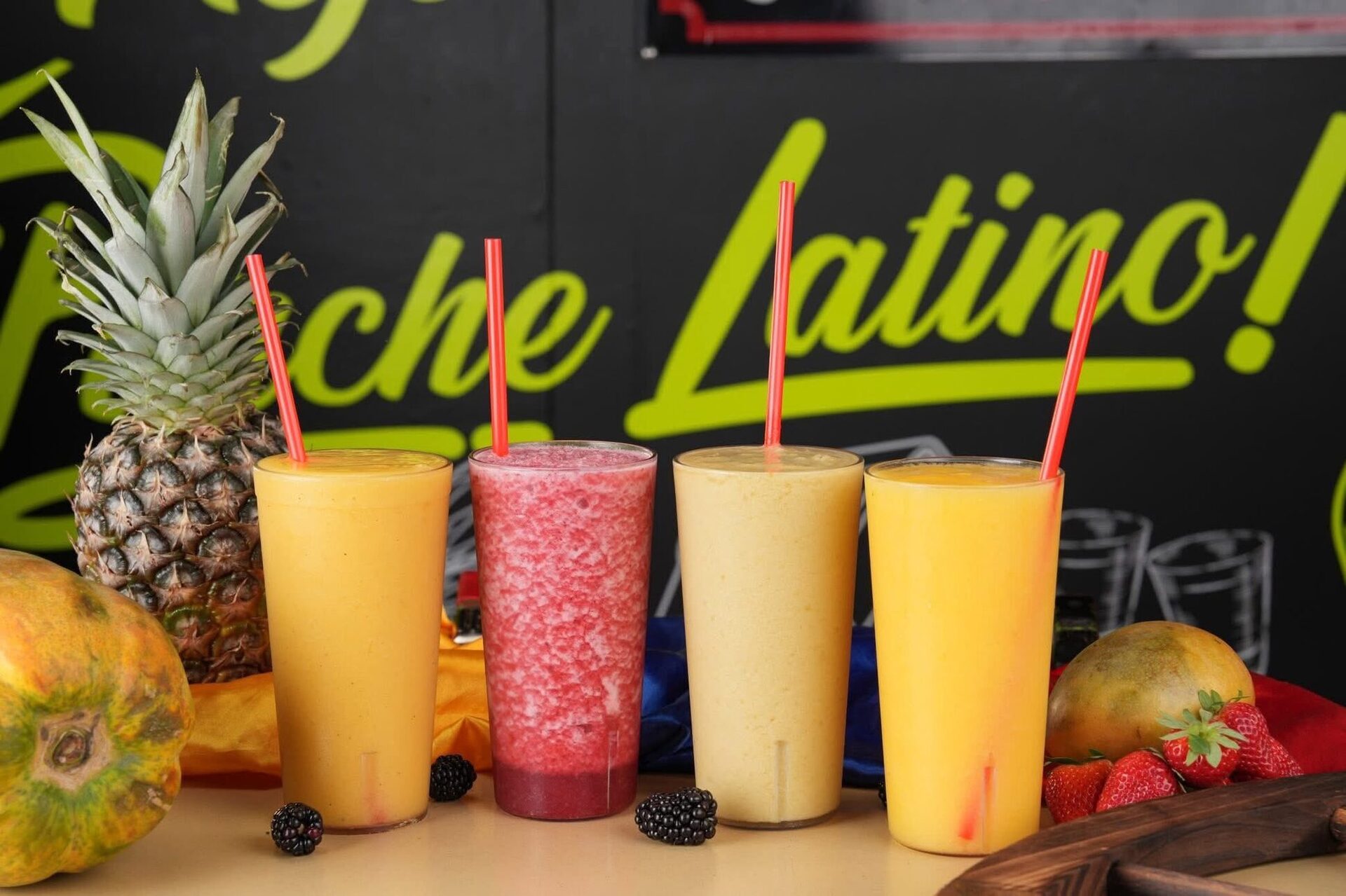 A row of fresh tropical juices in front of a neon-green mural
