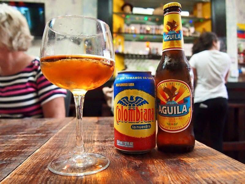 Colombiana soda, Águila beer and a glass on a wooden bar