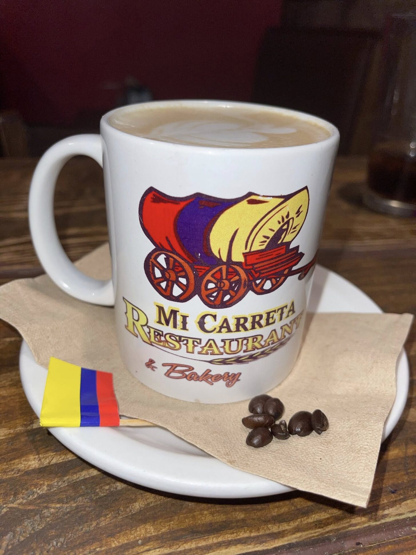 Café con leche in a Mi Carreta mug with a Colombian flag napkin and coffee beans